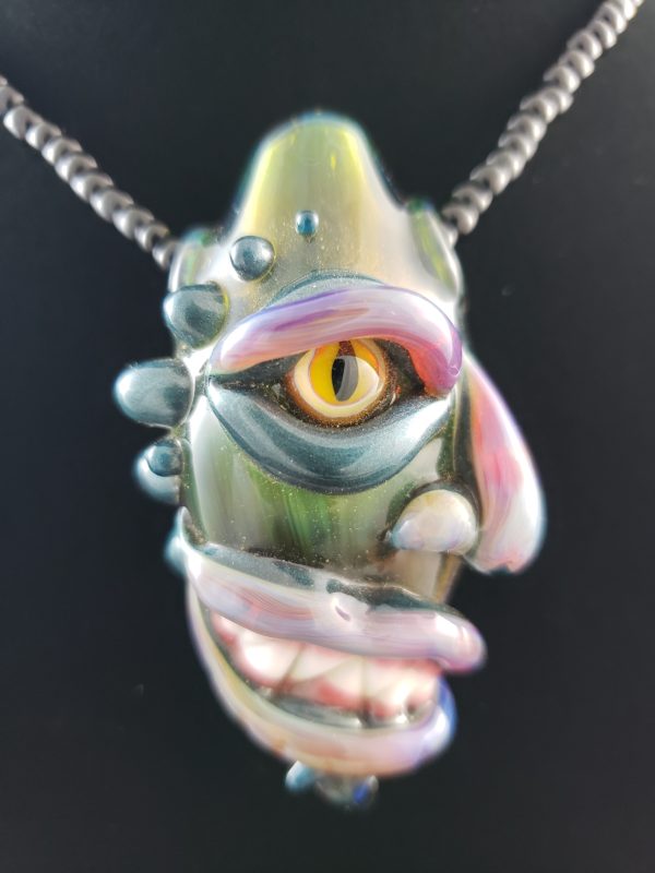 green and purple glass creature face pendant with yellow dragon cat eye