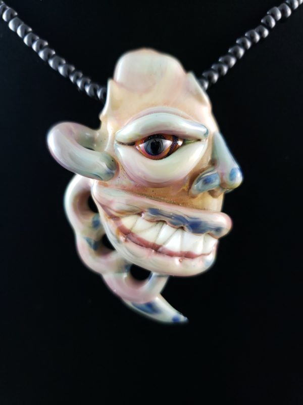 Blown glass creature face pendant side view with eye nose and mouth with teeth