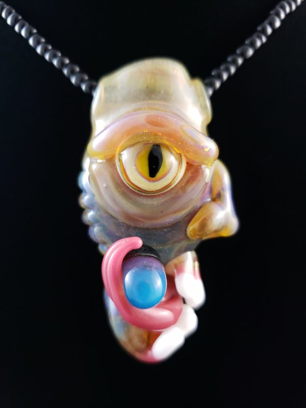 glass creature pendant with yellow cat eye and black and blue pill on tongue