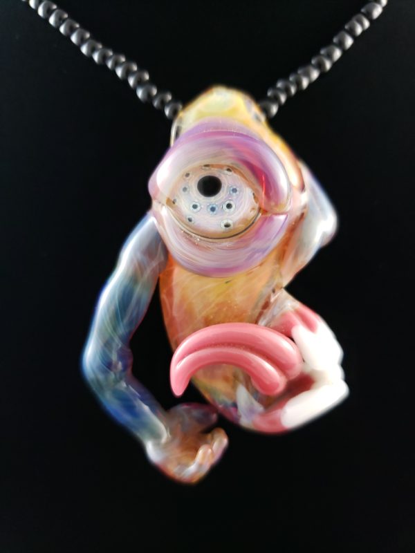 One blue armed glass creature pendant with tongue teeth and hand eye is purple with blue speckles body is orange